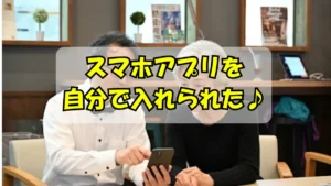 スマホアプリを入れることができて喜んでいるシニア女性とそれを教えているスマホ講師